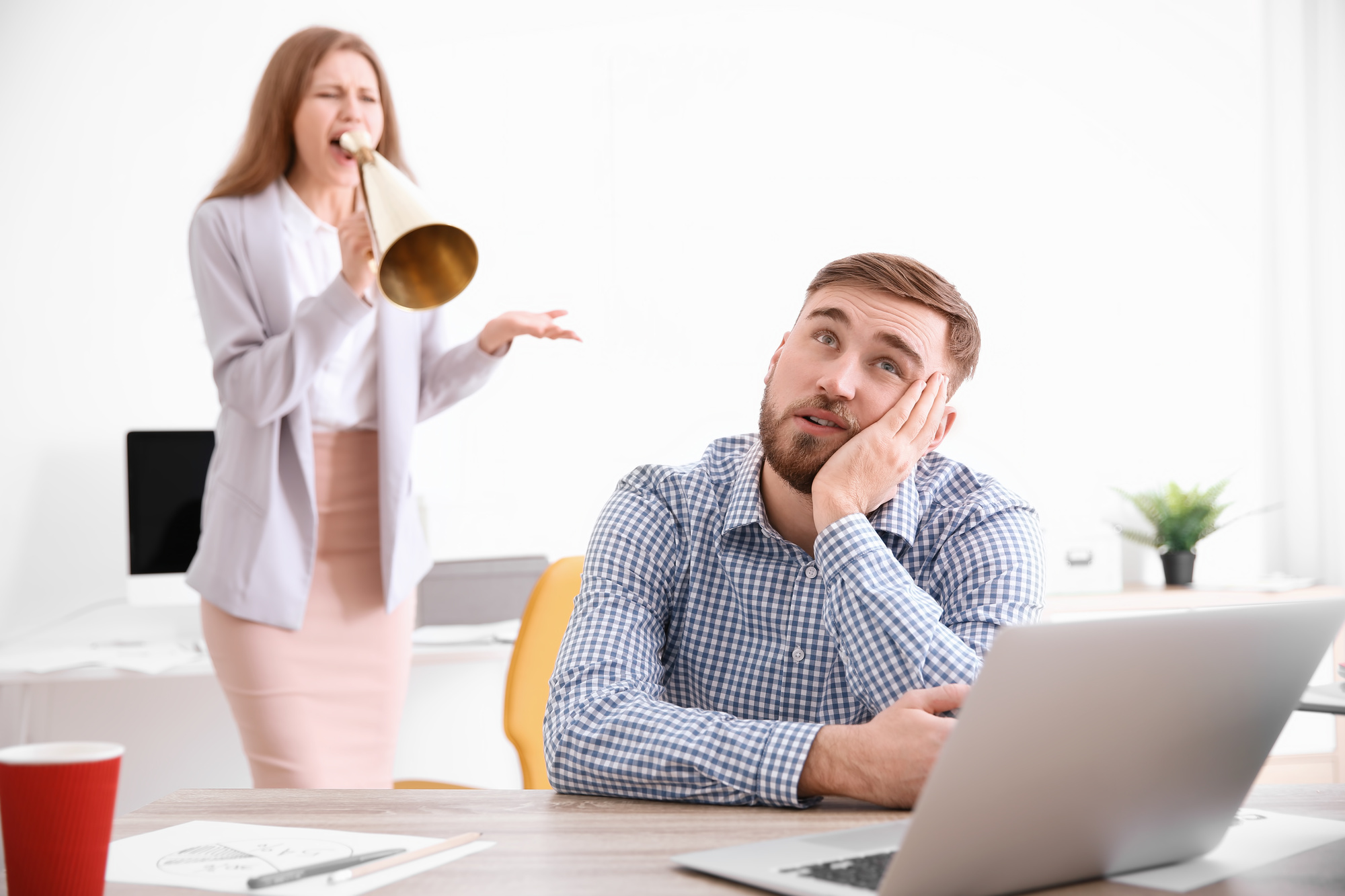 Angry boss with megaphone screaming at employee in office