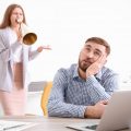 Angry boss with megaphone screaming at employee in office